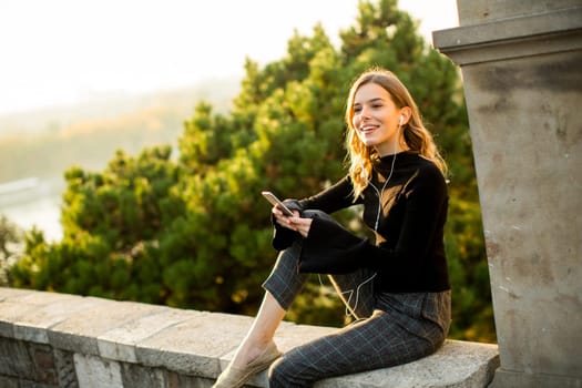 Portrait of young woman holding mobile phone while sitting on the wall