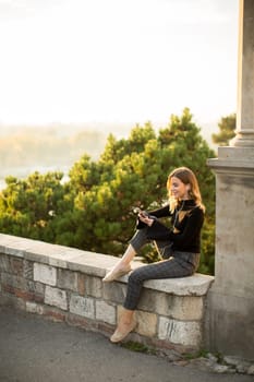 Portrait of young woman holding mobile phone while sitting on the wall