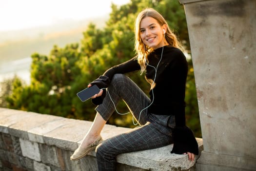 Portrait of young woman listens to music from a mobile phone outside