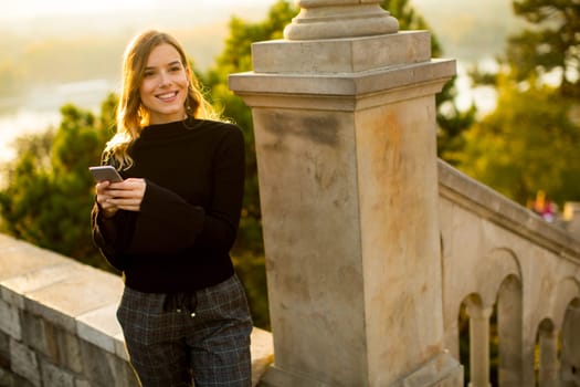 Portrait of young woman holding mobile phone while standing on the old stairs in the park