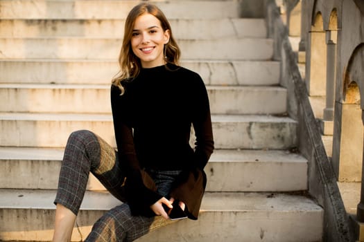 Trendu young woman with mobile phone sitting at stairs outdoor