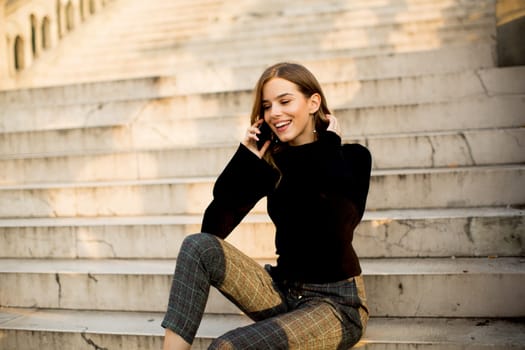 Trendu young woman with mobile phone sitting at stairs outdoor