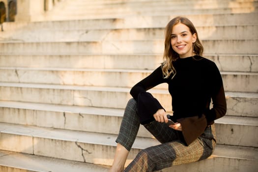 Trendu young woman with mobile phone sitting at stairs outdoor