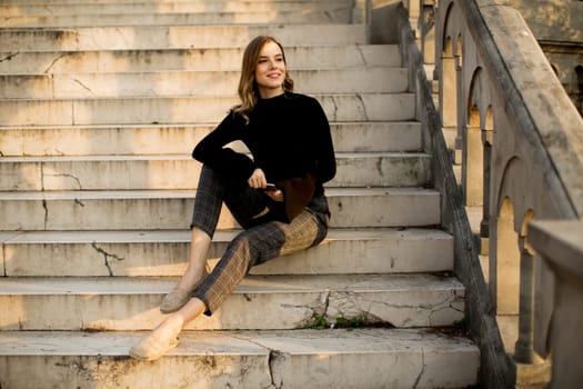 Trendu young woman with mobile phone sitting at stairs outdoor