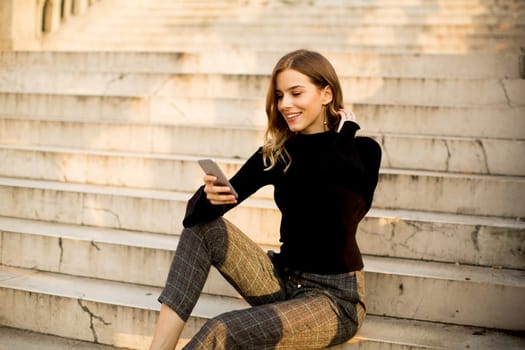Trendy young woman with mobile phone sitting at stairs outdoor