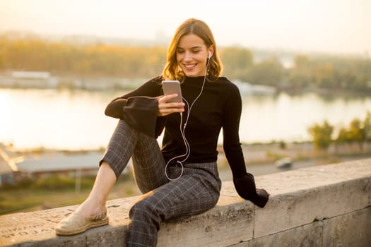 Trendy young woman listening music from smartphone outdoor at sunset
