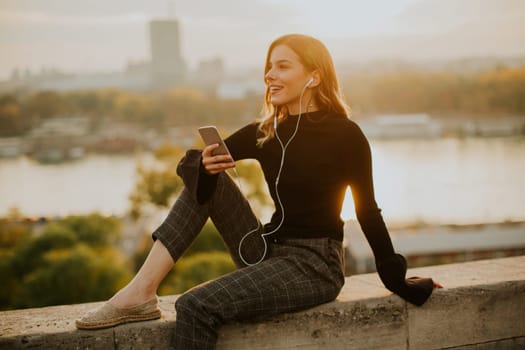 Trendy young woman listening music from smartphone outdoor at sunset