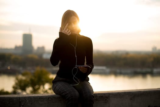 Portrait of trendy young woman listening music from smartphone outdoor at sunset