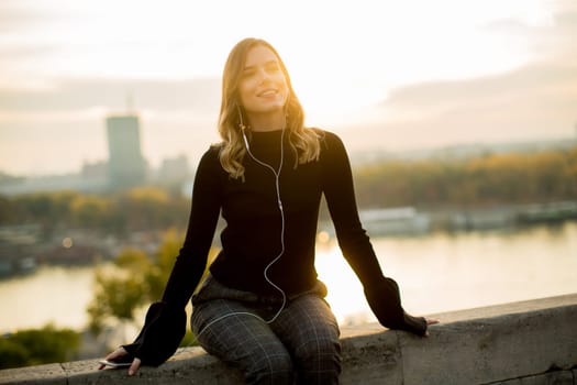 Trendy young woman listening music from smartphone outdoor at sunset