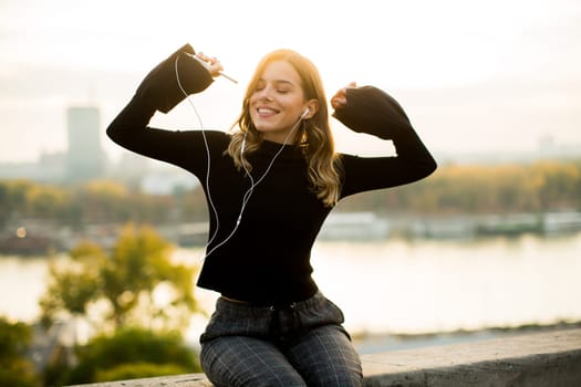 Trendy young woman listening music from smartphone outdoor at sunset