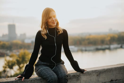 Portrait of trendy young woman listening music from smartphone outdoor at sunset
