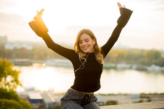 Trendy young woman listening music from smartphone outdoor at sunset