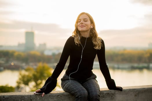 Portrait of trendy young woman listening music from smartphone outdoor at sunset
