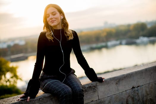 Trendy young woman listening music from smartphone outdoor at sunset