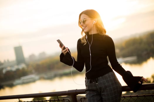 Trendy young woman listening music from smartphone outdoor at sunset
