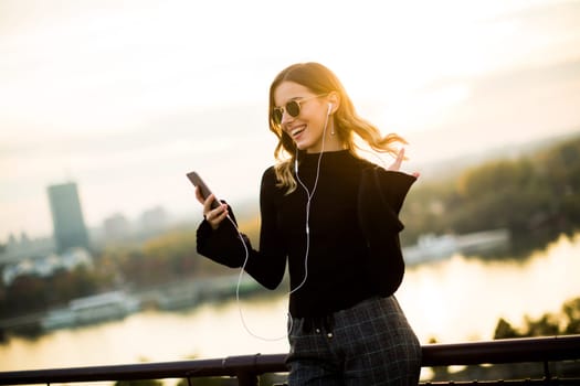 Trendy young woman listening music from smartphone outdoor at sunset