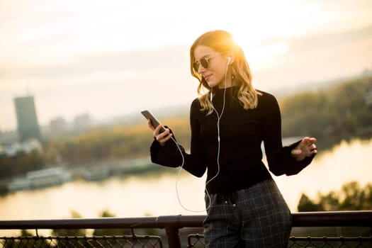 Trendy young woman listening music from smartphone outdoor at sunset