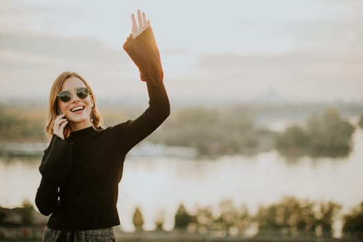 Portrait of young woman holding mobile phone while standing on walkway by the river
