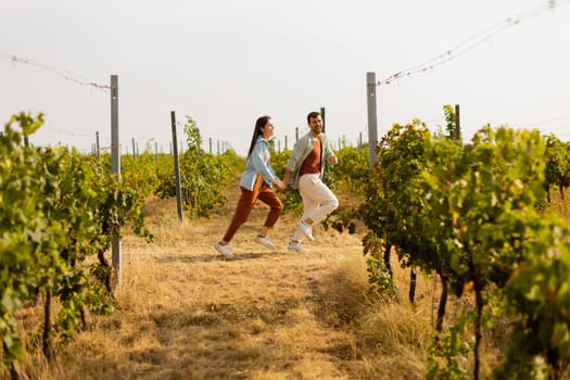 Young couple enjoys a carefree moment as they run through rows of verdant grapevines, basking in the warm sunlight of an idyllic afternoon in the vineyard