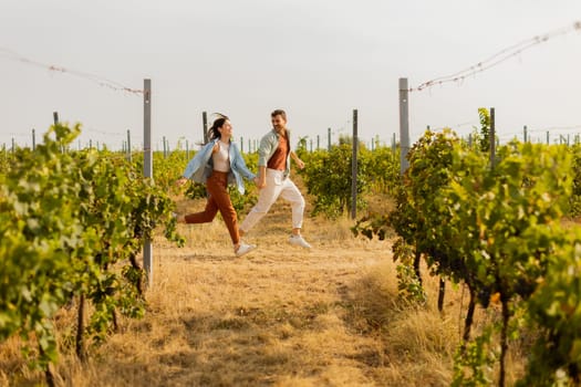 Young couple enjoys a carefree moment as they run through rows of verdant grapevines, basking in the warm sunlight of an idyllic afternoon in the vineyard