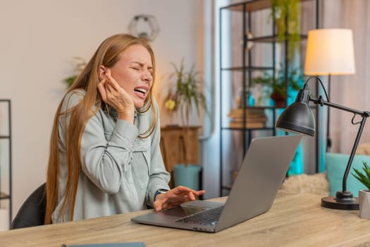 Sick mature Caucasian businesswoman freelancer sitting at home office table feeling ear pain, unhappy irritated woman or student. Furuncle, earache, shingles, eczema, ear disease, otitis concept.