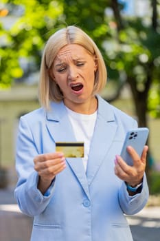Frustrated businesswoman discovered fraud while checking credit card on mobile phone standing on city street. Sad woman employer became a victim of deception, money had been stolen from her account.