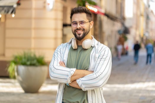 Portrait of happy smiling Caucasian young man looking at camera, resting, relaxation feel satisfied glad expression of good news outdoors. Bearded tourist on urban city street. Town lifestyles