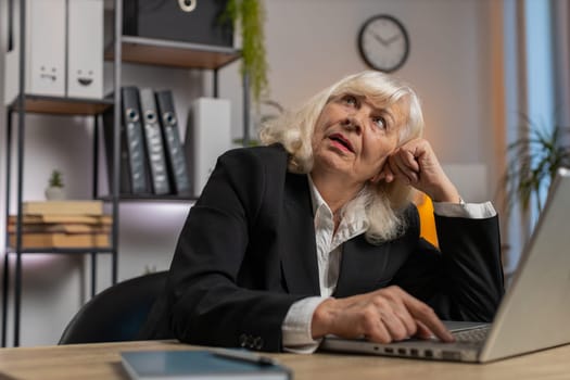 Exhausted tired Caucasian woman freelancer workaholic girl. Bored sleepy elderly businesswoman working on laptop computer yawns, leaning on hand at home office desk. Employment, occupation, workless.