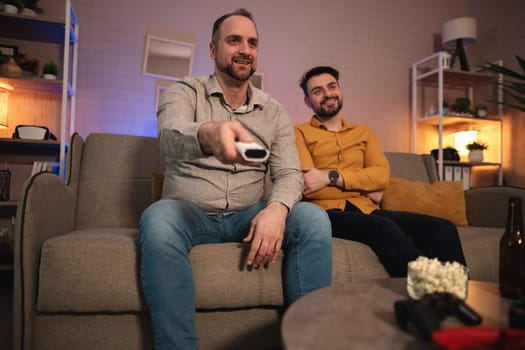 Two friends are comfortably seated on a sofa, laughing and enjoying their favorite movie together in a cozy, warmly lit living room. The atmosphere is relaxed and inviting.