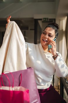 A woman joyfully chats on the phone while holding a sweater.