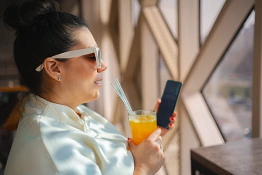Relaxing with a citrus drink and smartphone by the sunny window.