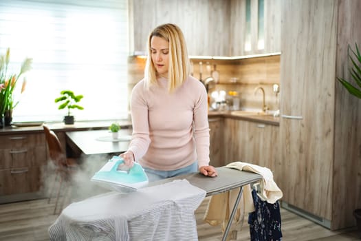 A woman steams a shirt at an ironing board in stylish decor.