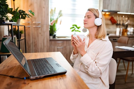 A woman enjoys a peaceful moment with headphones and a comforting drink.