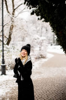 Pretty young woman in warm clothes enjoying in snow with takeaway coffee cup