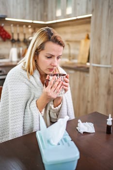 A woman wrapped in a blanket enjoys tea while recovering at home.