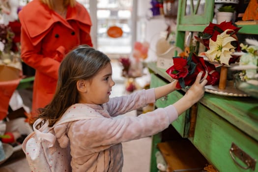 Excited and curious, a young girl wearing a cozy sweater examines vibrant flowers inside a quaint local shop adorned with fall decorations.