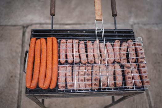Juicy sausages and bright hot dogs cook over an open flame outdoors.