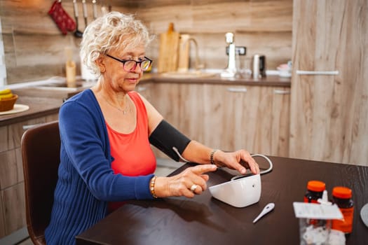 A senior woman checks her blood pressure while seated in her stylish kitchen.