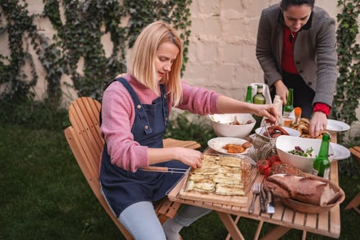 Two women share laughter and food while preparing a delicious meal outdoors.