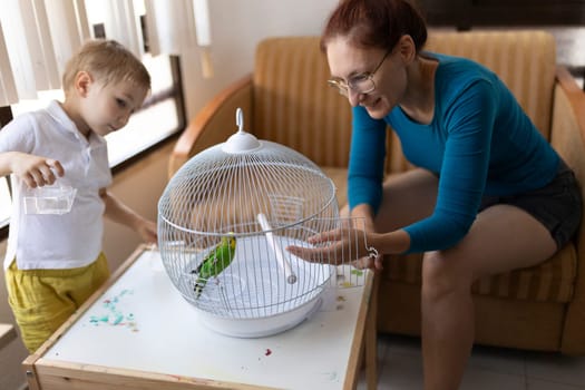 Mother and son interacting with their pet budgie in its cage, creating a heartwarming scene of family and pet bonding