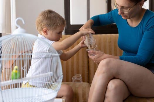 Mother and son pouring birdseed into a small bowl to feed their pet parakeet