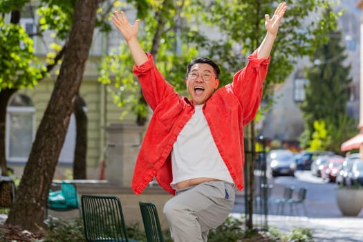 Asian middle-aged man shouting celebrating success winning goal achievement good news lottery jackpot casino luck victory career outdoors. Chinese guy on urban city street. Town lifestyles. Horizontal