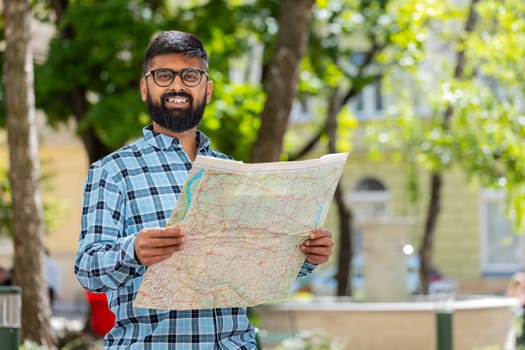 Indian young man tourist exploring city street, sightseeing holding paper map, check direction searching way looking for the route outdoors. Travel concept. Hispanic guy. Town lifestyles. Horizontal