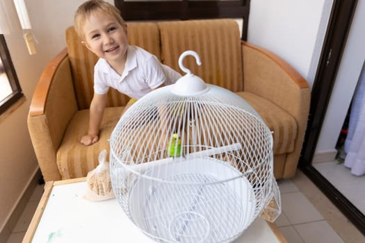 Happy child interacting with a small green parrot inside its white cage