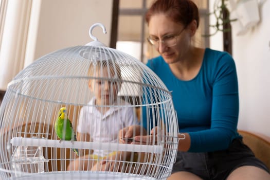 Mother and son taking care of their pet parrot inside its cage at home