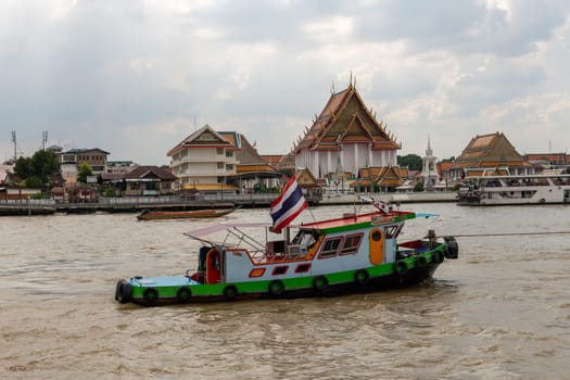 A colorful boat cruises smoothly on a scenic river, showcasing the vibrant Thai culture and architecture