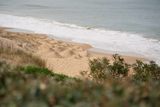 Waves gently lap at the sandy beach of Biscarrosse while soft dunes rise in the background, creating a serene coastal environment on a calm day.