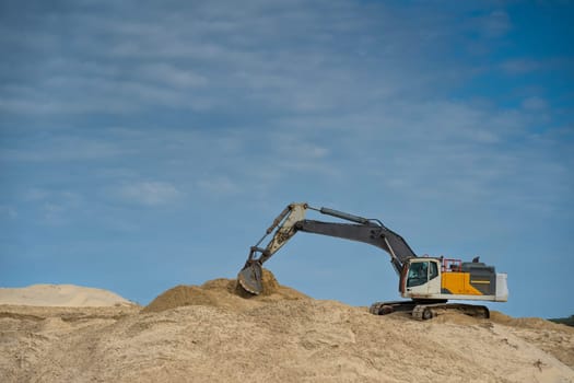 Heavy machinery is actively moving sand along the coastline under a clear blue sky, focusing on erosion control efforts during daylight hours in a coastal area.