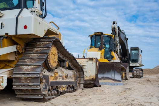 Heavy machinery is positioned along the sandy coastline, actively involved in erosion control and coastal protection efforts under a cloudy sky.