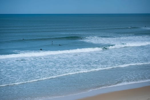 Two surfers navigate the rolling waves at Biscarrosse Beach during a serene day. The calm waters reflect the azure sky, creating a perfect surfing environment.